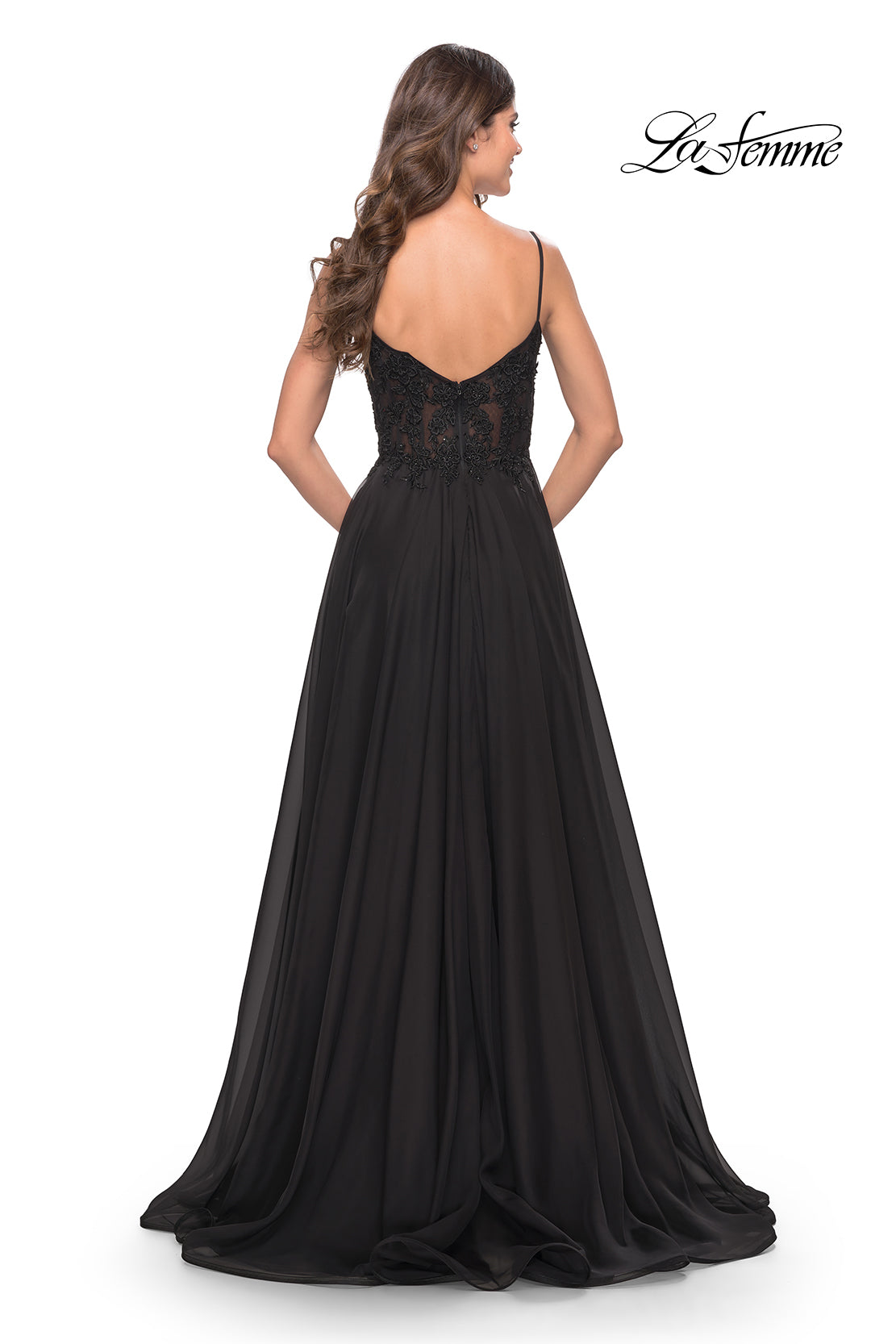 A woman models the La Femme Long A-Line Prom Dress with a sheer lace bodice, thin straps, and a flowing black skirt, shown from the back. The La Femme logo is in the top right corner.
